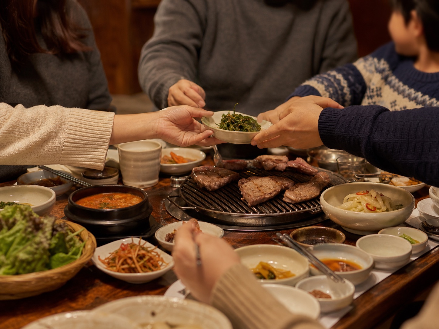Friends and family passing Korean side dishes around a shared table