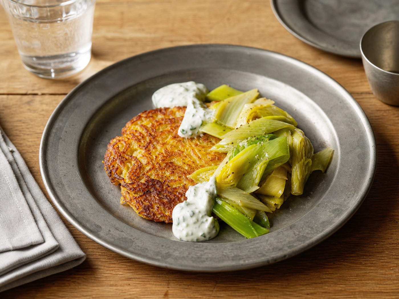 Rösti with braised leek and herb cream on a pewter plate